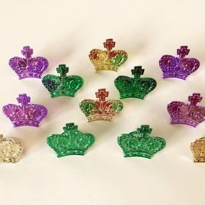 May include: Twelve metallic crowns in gold, green, and purple. The crowns are decorated with fleur-de-lis and a cross on top.