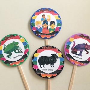 May include: Four colorful cupcake toppers featuring illustrations from the children's book "Brown Bear, Brown Bear, What Do You See?" The toppers feature a green frog, a black sheep, a purple cat, and a group of children.