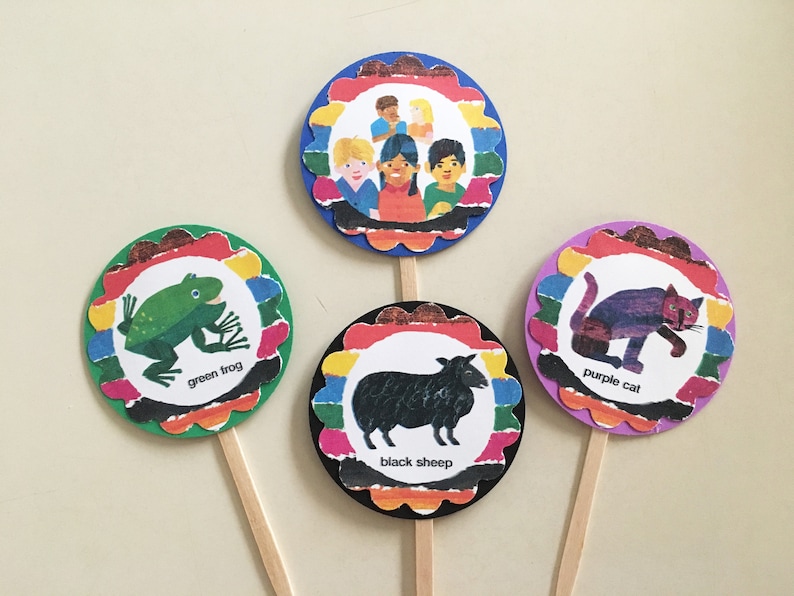 May include: Four colorful cupcake toppers featuring illustrations from the children's book "Brown Bear, Brown Bear, What Do You See?" The toppers feature a green frog, a black sheep, a purple cat, and a group of children.