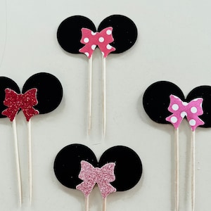 Puede incluir: Tres juegos de orejas de ratón de fieltro negro con lazos rosas. Los lazos tienen diferentes patrones: lunares, purpurina y rosa sólido.