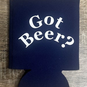 Pode incluir: Um refrigerador de latas de neopreno azul marinho com texto branco que diz "Got Beer?"