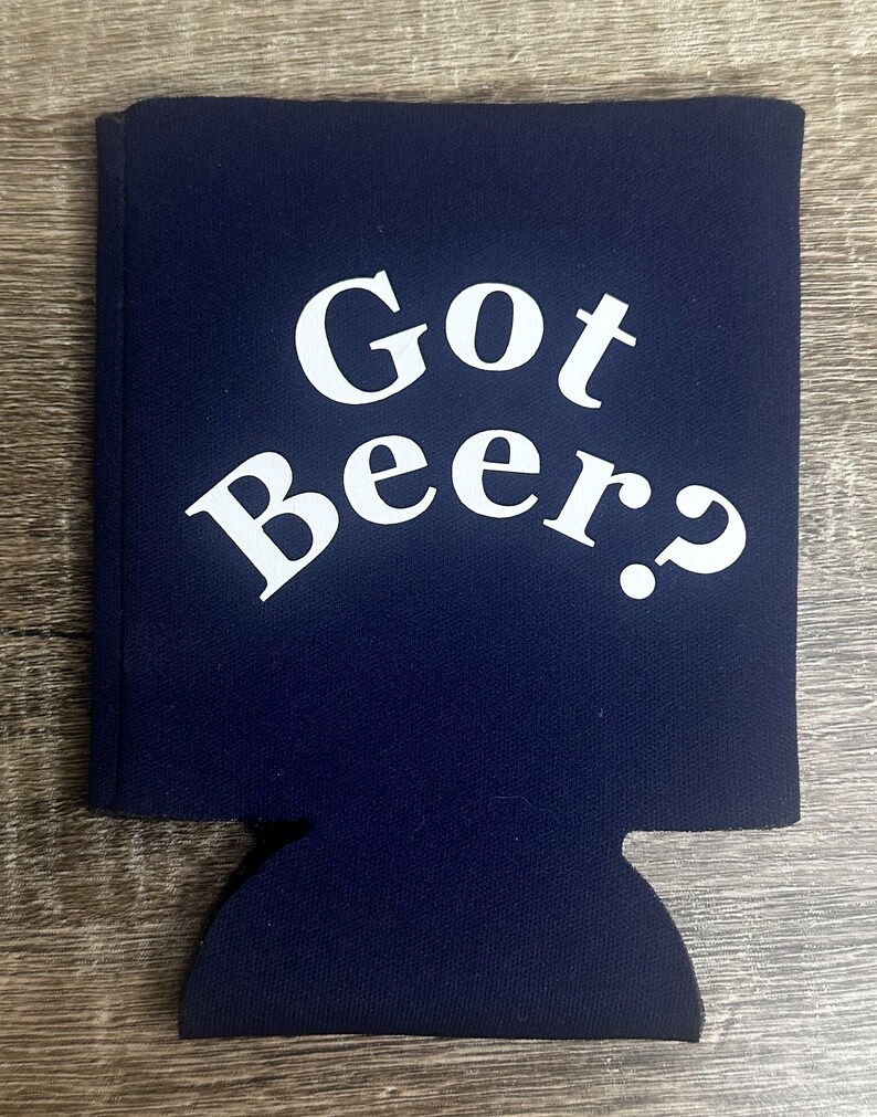 Pode incluir: Um refrigerador de latas de neopreno azul marinho com texto branco que diz "Got Beer?"