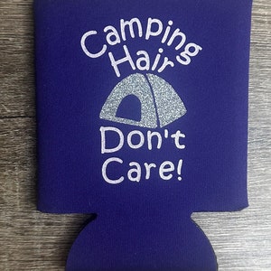 Pode incluir: Resfriador de latas de neopreno roxo com um design branco que diz "Camping Hair Don't Care!" com um gr&aacute;fico de barraca de glitter prata.