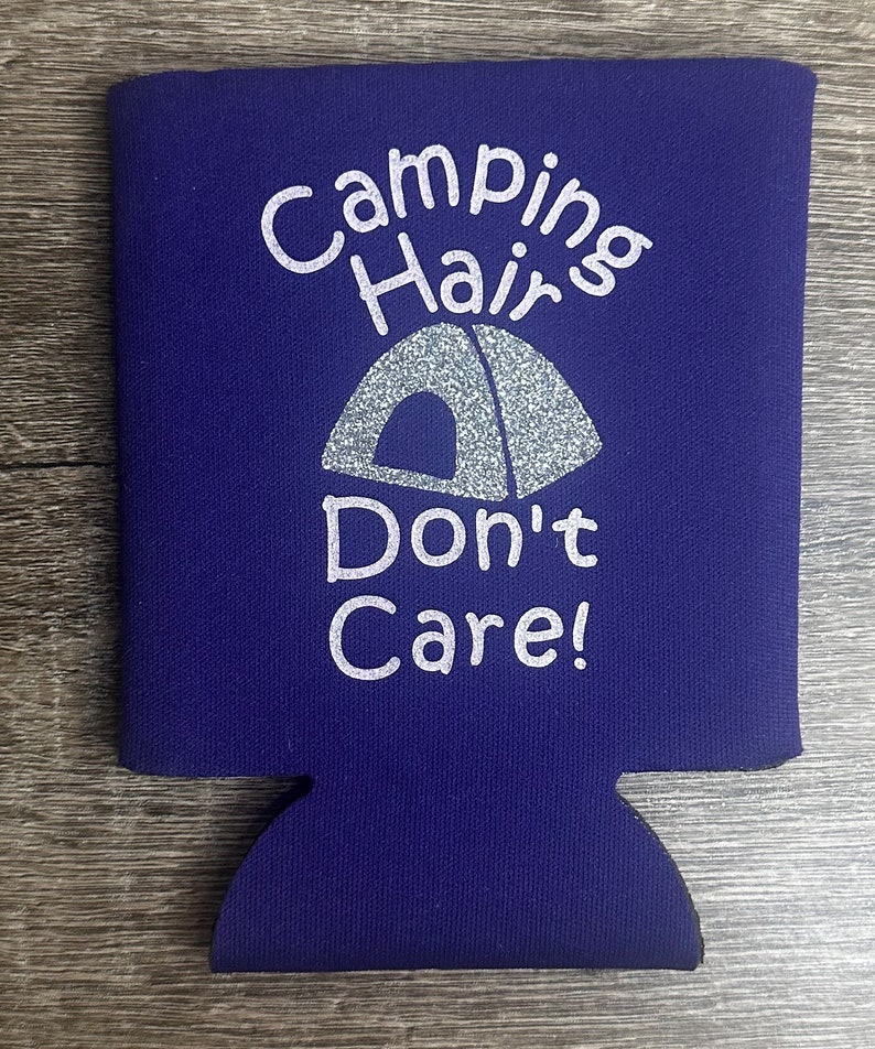 Pode incluir: Resfriador de latas de neopreno roxo com um design branco que diz "Camping Hair Don't Care!" com um gr&aacute;fico de barraca de glitter prata.