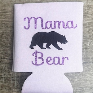 Pode incluir: Um refrigerador de latas branco com um design de purpurina roxo que diz "Mama Bear" com uma silhueta de urso preto.