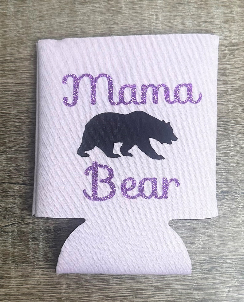 Pode incluir: Um refrigerador de latas branco com um design de purpurina roxo que diz "Mama Bear" com uma silhueta de urso preto.