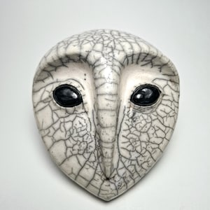 Könnte beinhalten: Eine weiße Keramik-Eulenmaske mit schwarzen Augen und einer craquelé-Glasur.