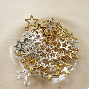 Könnte beinhalten: Eine Schale gefüllt mit goldenen und silbernen sternförmigen Charms mit einer Öse oben. Die Charms sind perfekt für die Schmuckherstellung oder zum Basteln.