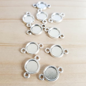 Könnte beinhalten: Zehn runde, silberfarbene Metall-Bezel-Einstellungen mit jeweils zwei Sprungringen. Die Bezel sind so konzipiert, dass sie einen runden Cabochon aufnehmen können.