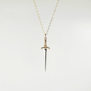 May include: A gold chain necklace with a silver sword pendant. The sword has a gold hilt and a pointed tip.