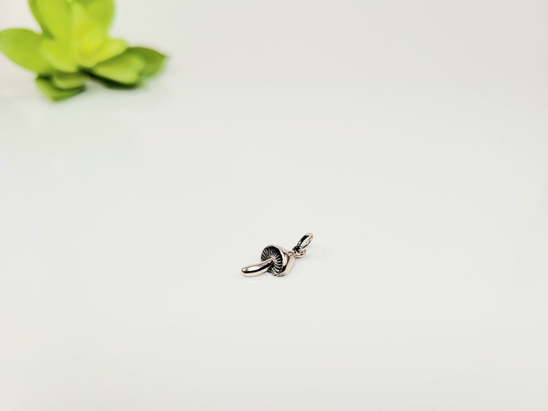 Pode incluir: Um amuleto de prata em forma de cogumelo. O amuleto tem um design detalhado e um la&ccedil;o para prender a um colar ou pulseira.