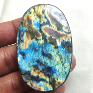 May include: Oval-shaped labradorite gemstone with a polished surface. The stone displays a vibrant play of color, with blues, greens, and oranges swirling across the surface. Dark gray inclusions add contrast to the iridescent effect. A natural gemstone for jewelry making.