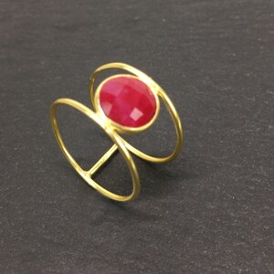 May include: Gold ring with a red gemstone set in a double circle design.
