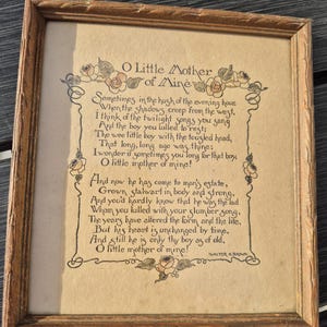 May include: A framed vintage print with the poem "O Little Mother of Mine" in elegant script. The artwork features floral embellishments and is encased in a wooden frame. The text is in black ink on a tan background.