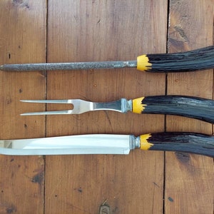 May include: A set of three kitchen utensils with black and yellow handles. The set includes a carving knife, a fork, and a sharpening steel.