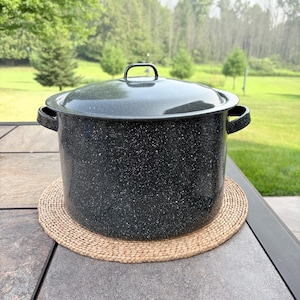 May include: A large, cylindrical black stockpot with a speckled white finish, featuring two side handles and a matching lid with a central handle. The pot has a smooth, glossy surface and is constructed from metal with an enamel-like coating.