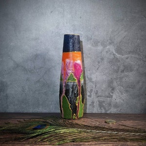 Può includere: Un vaso alto, nero e verde, con un design unico che presenta accenti rosa e arancioni. Il vaso è decorato con un motivo di forme e linee astratte.