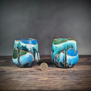 Può includere: Due tazze in ceramica dipinte a mano in blu e verde con dettagli dorati. Le tazze sono su una superficie di legno.