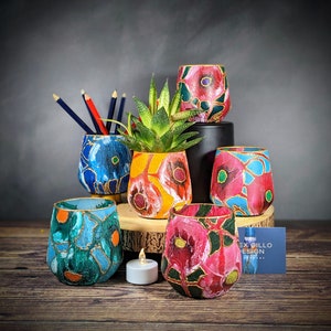 May include: Six colorful hand-painted ceramic planters with gold accents. The planters are arranged in a group on a wooden surface. The planters feature floral designs in shades of blue, red, yellow, and green.