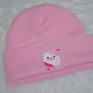 May include: Pink knitted beanie with a white embroidered cartoon cow with pink accents and hearts.