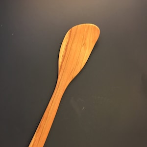 May include: A wooden spatula with a light brown color and a slightly curved shape.