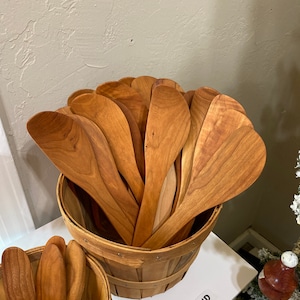May include: A basket filled with wooden spoons, with the label "LEFT HAND" on a white surface.