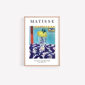 May include: A painting by Henri Matisse titled "Les Coucous, Tapis Bleu Et Rose" depicting a vase of yellow flowers on a blue and white patterned tablecloth. The vase is white with blue and black designs. The background is a blue wall with a red door and a small painting on the wall.