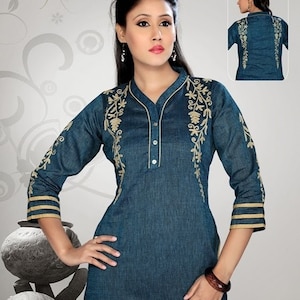 Puede incluir: Una camisa de manga larga azul turquesa con cuello mandarín y bordados dorados. La camisa tiene cierre de botón y un dobladillo ligeramente curvo.