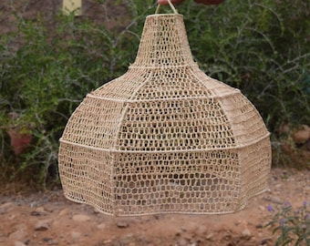 May include: A beige woven lampshade with a bell shape. The lampshade is made from a natural fibre and features an open weave design. It is suspended by a loop at the top, suitable for hanging, and is approximately 30 cm in diameter.