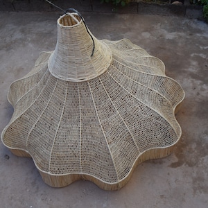 May include: A large, woven, light brown, lampshade with a scalloped edge. The lampshade is made of natural materials and has a unique, organic shape.