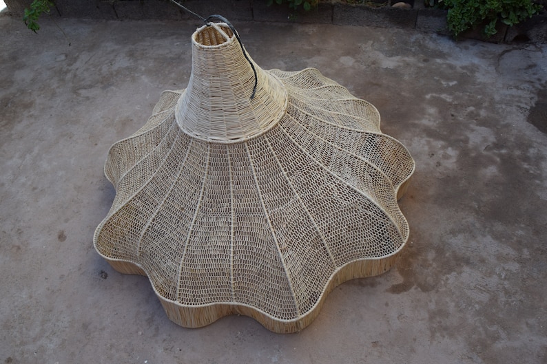 May include: A large, woven, light brown, lampshade with a scalloped edge. The lampshade is made of natural materials and has a unique, organic shape.