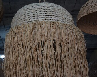 May include: A woven lampshade with a fringe made of natural fibers. The lampshade is white and the fringe is a light brown color.