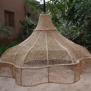 May include: A large, woven, beige lampshade with a unique, wavy, scalloped bottom edge. The lampshade is made of natural materials and has a rustic, handcrafted look.