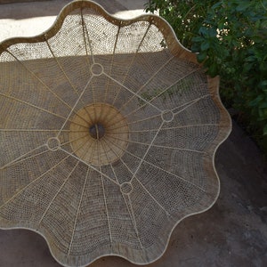 May include: A large, round, woven basket with a scalloped edge. The basket is made of natural materials and has a intricate pattern of woven strands.