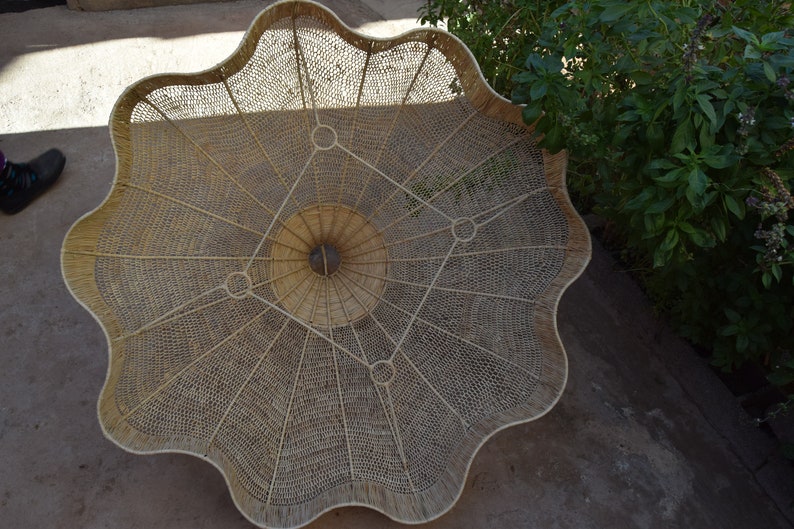 May include: A large, round, woven basket with a scalloped edge. The basket is made of natural materials and has a intricate pattern of woven strands.