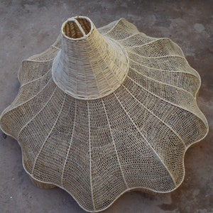 May include: A large, white, woven lampshade with a scalloped edge. The lampshade is made of a natural material, possibly rattan or bamboo.