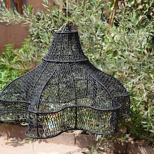 Puede incluir: Una pantalla de lámpara de forma de estrella, negra y tejida, que cuelga de un cordón. La pantalla está hecha de un delicado y complejo patrón de material tejido.