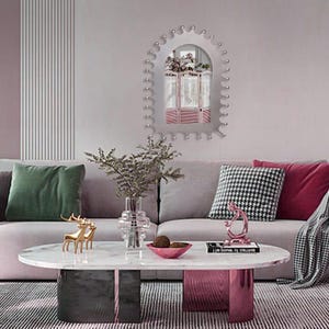 Op de afbeelding: Een moderne woonkamer met een grijze bank, decoratieve kussens en een marmeren salontafel. Een decoratieve spiegel met een roze kamerscherm is aan de muur bevestigd. Gouden hertenbeeldjes en een roze kom voegen kleuraccenten toe.