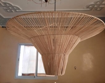 May include: A large, round, woven lampshade made of natural fibers hangs from the ceiling. The lampshade is light brown in color and has a conical shape.