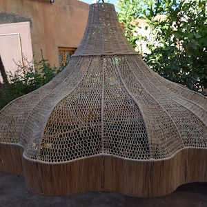 May include: A large, woven, light brown lampshade with a scalloped edge. The lampshade is made of a natural material, possibly straw or bamboo.