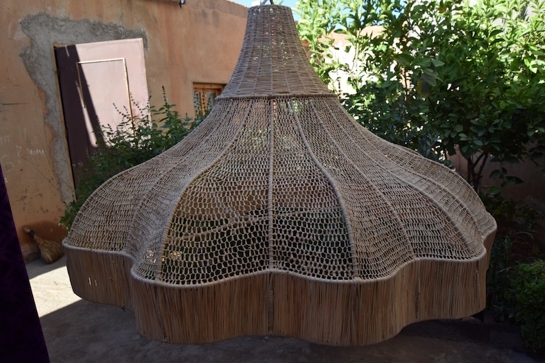 May include: A large, woven, light brown lampshade with a scalloped edge. The lampshade is made of a natural material, possibly straw or bamboo.