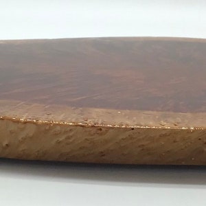 May include: A large, round wooden serving tray with a natural wood finish. The tray has a unique, irregular shape and a smooth, polished surface.