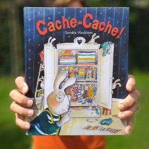 Könnte beinhalten: Ein Kinderbuch mit dem Titel "Cache-Cache!" von Sandra Vlasblom. Der Umschlag zeigt eine farbenfrohe Illustration eines Kaninchens, das aus einem Schrank schaut, während sich andere Kaninchen darin verstecken.