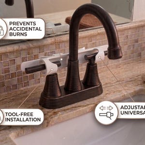 May include: A bronze-colored bathroom faucet with a white safety device installed. The device is designed to prevent accidental burns and offers tool-free installation and an adjustable, universal fit.