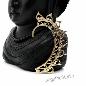 May include: Gold ear cuff with a delicate, intricate design. The cuff is shaped like a leaf and has a floral pattern. It is a statement piece that would add a touch of elegance to any outfit.