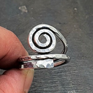 May include: A silver ring with a hammered finish and a spiral design. The ring is adjustable and can be worn on any finger.