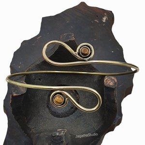 Op de afbeelding: Een gouden draad armband met twee bruine tijgeroogstenen. De armband is open en verstelbaar.