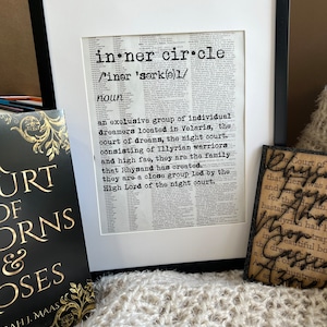 May include: A framed print of a dictionary definition of the term "inner circle" with the text "an exclusive group of individual dreamers located in Velaris, the court of dreams, the night court. consisting of Illyrian warriors and high fae, they are the family that Rhysand has created... they are a close group led by the High Lord of the night court."