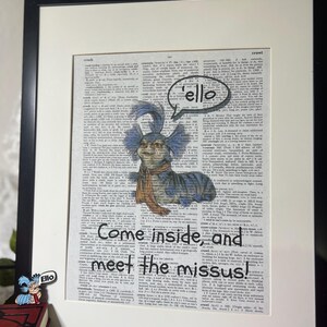 May include: Framed artwork featuring a whimsical illustration of a blue creature with a scarf, set against a vintage dictionary page. The artwork includes the text "'ello" in a speech bubble and "Come inside, and meet the missus!"