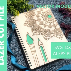 May include: A wooden notebook with a laser-cut mandala design and a green paintbrush and pencil design. The notebook has a spiral binding and is on a blue surface. The text "VECTOR MODEL" is at the top of the image and the text "SVG DXF AI EPS PDF" is at the bottom of the image.
